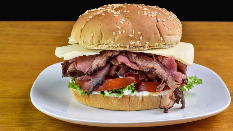 a roast beef sandwich with cheese, lettuce, tomato, and mayo on a sesame seed bun