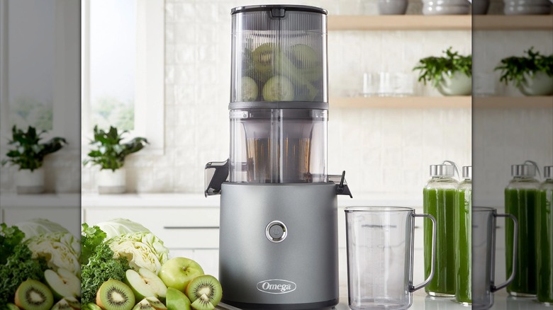 A gray juicer sits next to green fruit and vegetables, ready to make green juice.