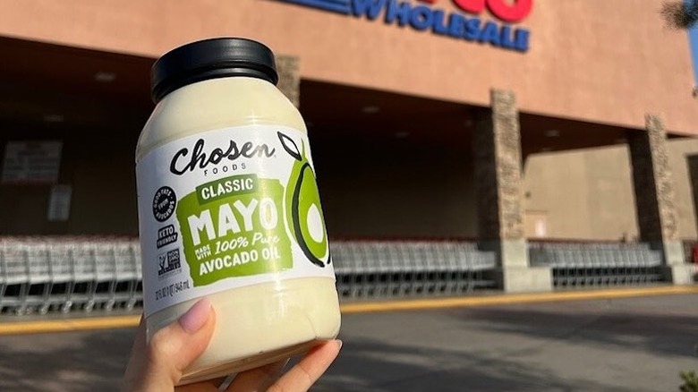 A hand holds up a jar of mayonnaise outside of a Costco.