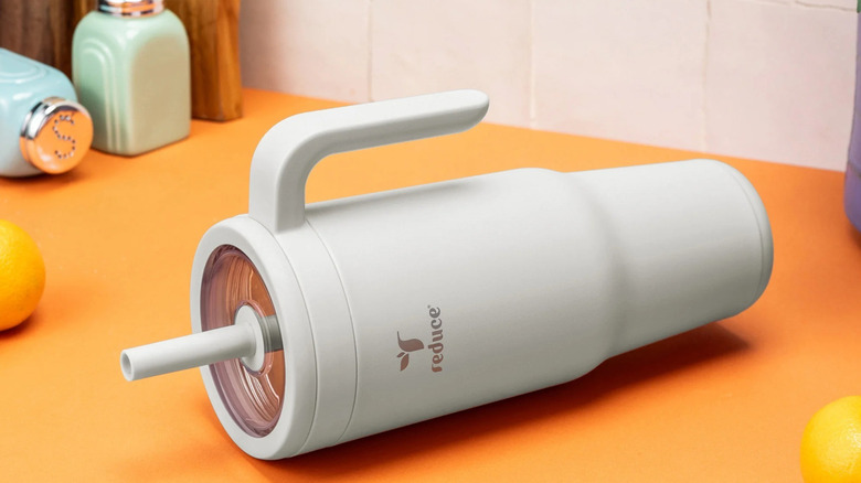 A white Reduce cup lies on its side on an orange countertop