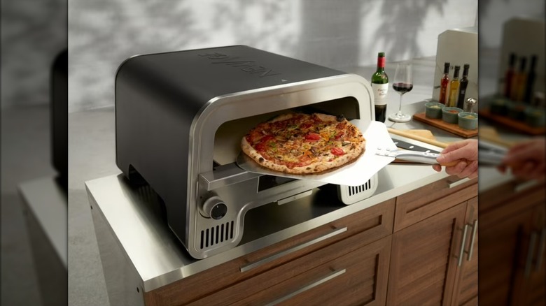 A hand removes a pizza from a NewAge Perfect Crust Pizza Oven