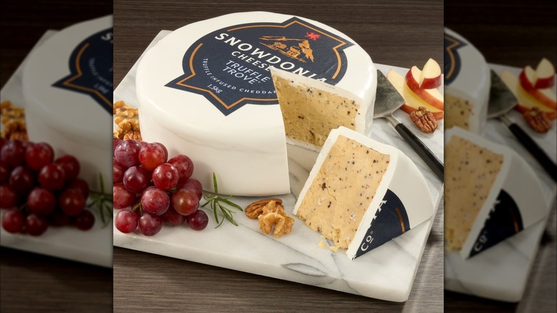 A wheel of cheese sits surrounded by fruit and nuts.