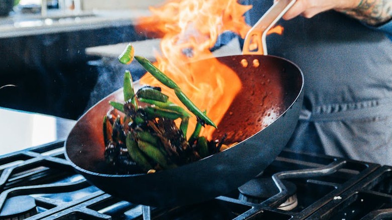 A cook handles a carbon steel wok on a stove.