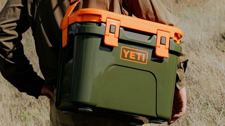 A hiker totes a cooler on their back.