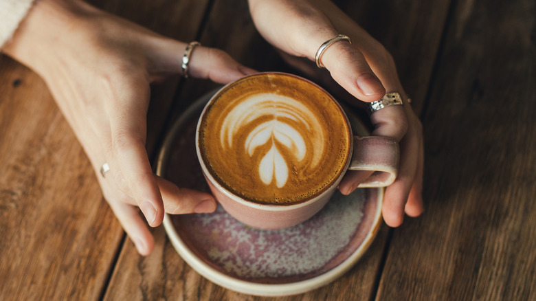 Hands cradling a cup of coffee with foam art