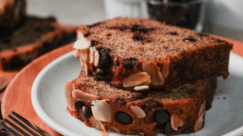 slices of banana bread with chocolate chips and some flaked nuts are stacked on a plate