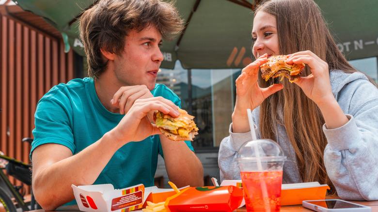 A young couple eat McDonald's burgers at an outdoor table