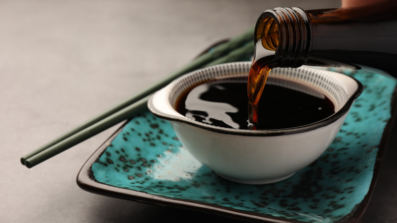 Soy sauce being poured into a small bowl on a table.
