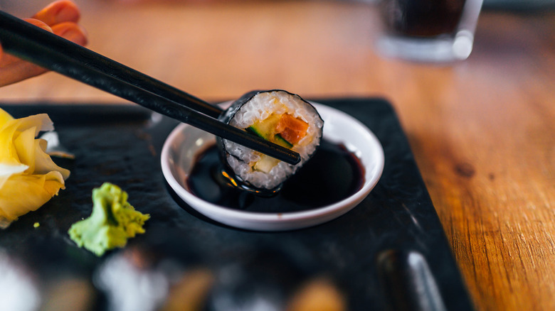 A person dipping sushi in soy sauce.