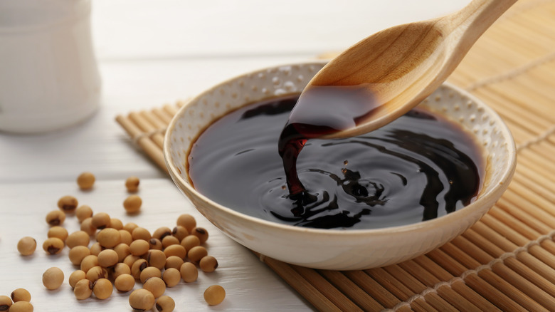 Soy sauce being taken from white a bowl using a wooden spoon.