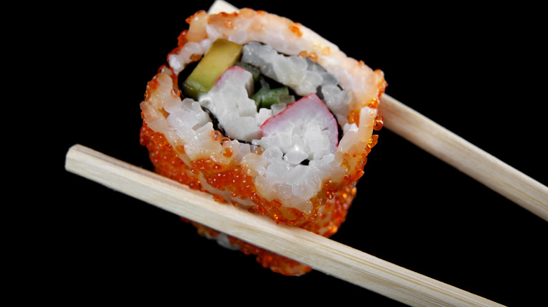 chopsticks holding California sushi roll