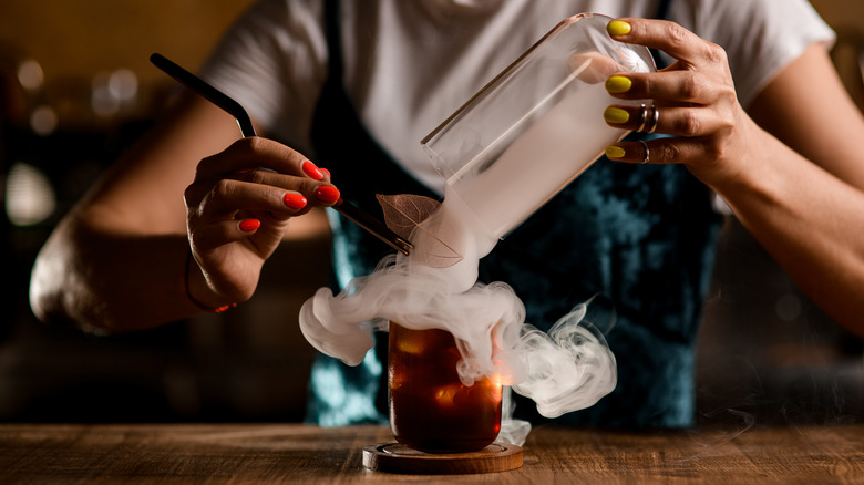 Making a smoked whiskey cocktail with a glass domed lid