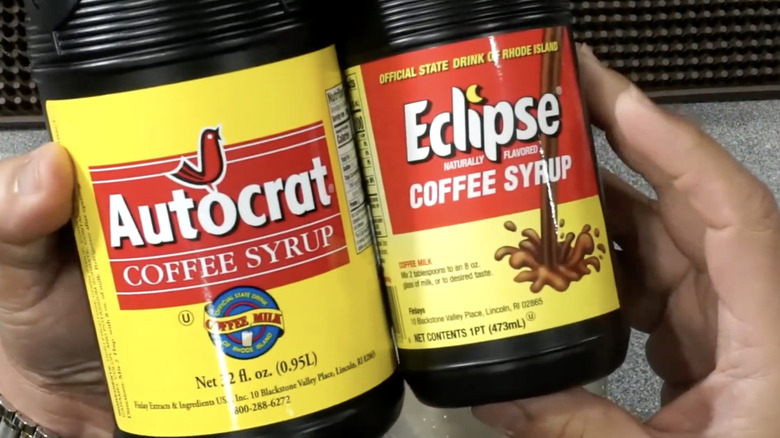 Hands hold two brands of coffee syrups for coffee cabinets.