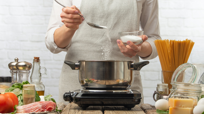 cook adding salt to boiling water for pasta