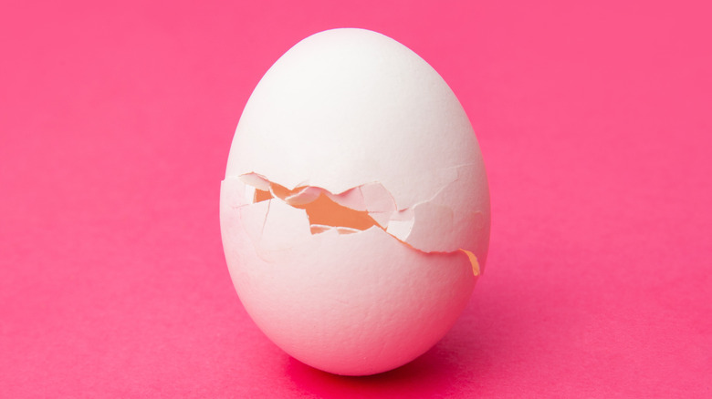 Cracked white egg on pink background