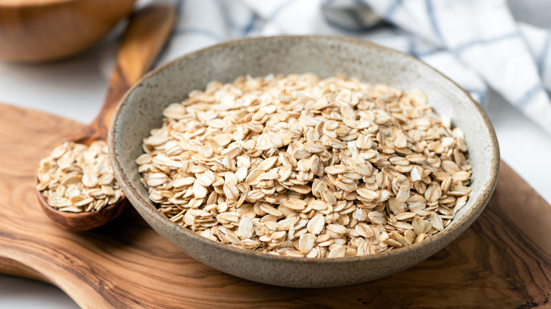 Bowl of oats with nearby wooden spoon of oats.