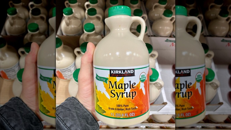 A hand holds a jug of Kirkland Signature Organic Maple Syrup in Costco