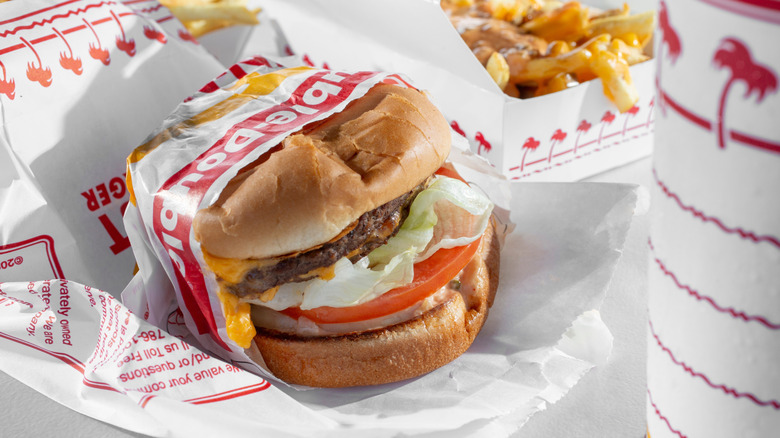 In N Out burger in paper wrapper with fries and a drink