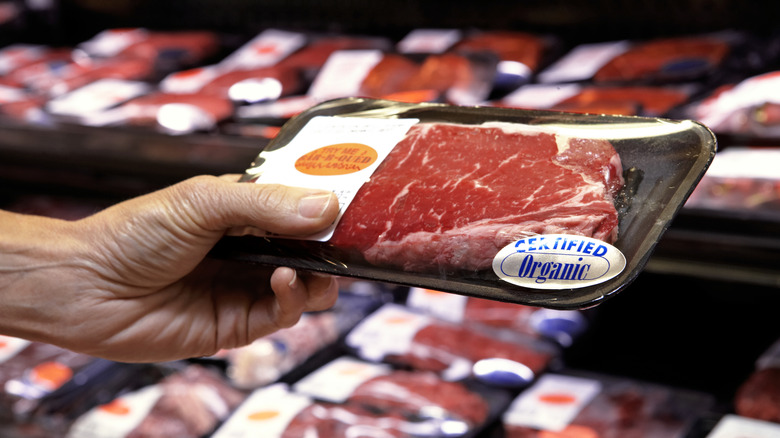 A person holding beef at a grocery store.