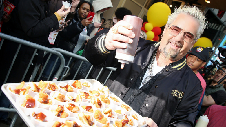 Guy Fieri holding a plate of chicken nuggets and sauce.