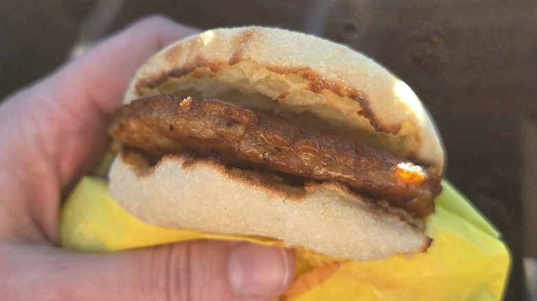 A hand holds a McMuffin in their car