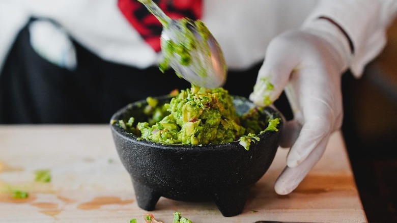 Gloved hands preparing tableside guacamole