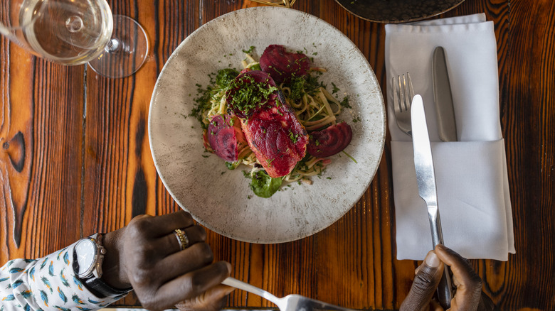 hands holding silverware over plate of food