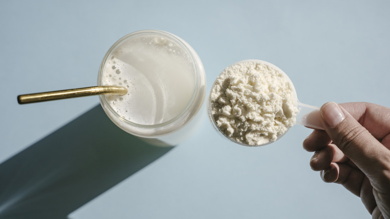 Scooping protein into a glass of milk with a metal straw