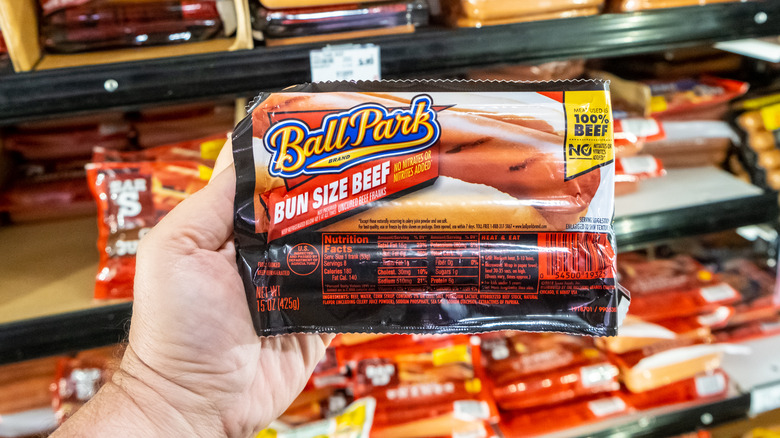 Customer holding packahge of Ball Park hot dogs in front of a display case