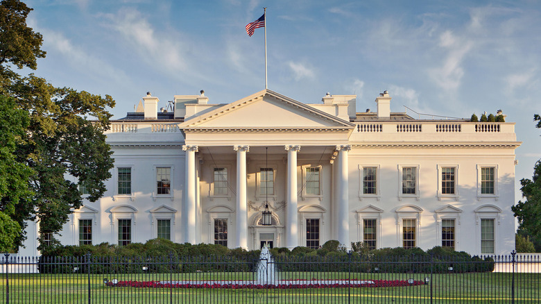 White House with an American flag on the roof and grass-covered White House lawn with a large fountain in the center