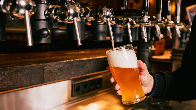 person holding a glass of beer while a stream of beer flows into it