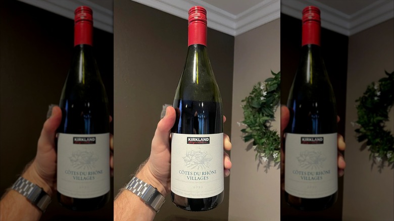 A hand holding Costco's Kirkland Signature Côtes du Rhône Villages bottle.