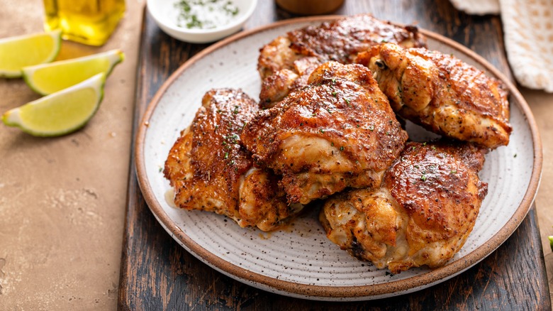 Perfectly cooked chicken thighs on a plate next to lime wedges