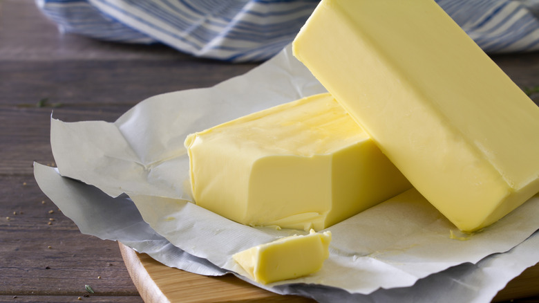 Two unwrapped and sliced blocks of butter on a wooden chopping board