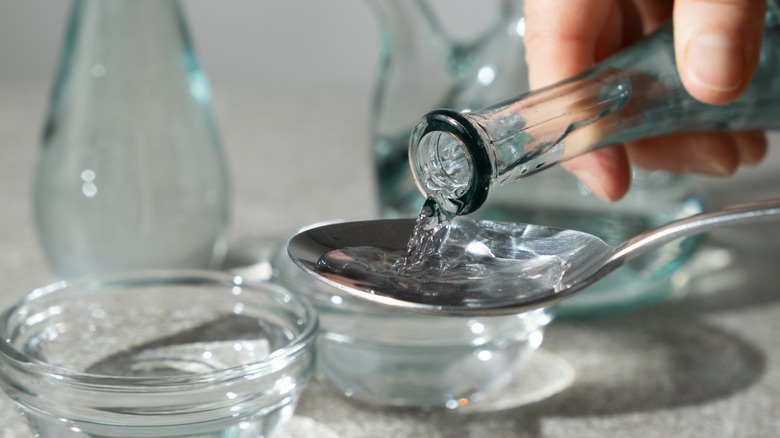 Someone pours white vinegar from a glass bottle into a spoon