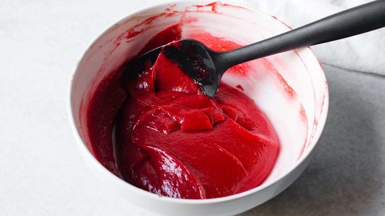 Red velvet cake batter sits in a white bowl with a black spoon