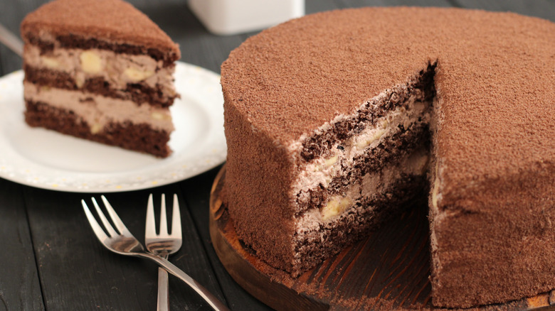 A rich chocolate and cream layer cake with a single piece removed on a plate in the background