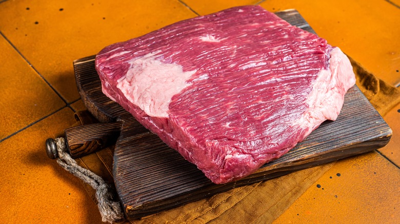 Whole piece of raw brisket on a cutting board on orange tiled surface