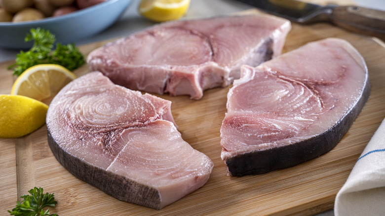 Raw swordfish steaks on wood cutting board with lemon and parsley 