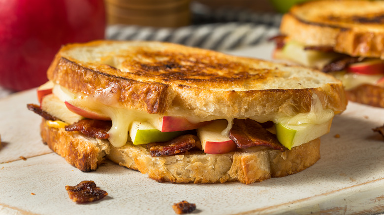 grilled cheese with apple and bacon on a white slab of wood