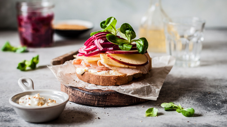 openface sandwich with sliced meat, apple, cheddar, pickled red onion, and microgreens on top