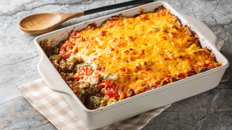 A cheese and meat casserole in a white baking dish next to a wooden spoon