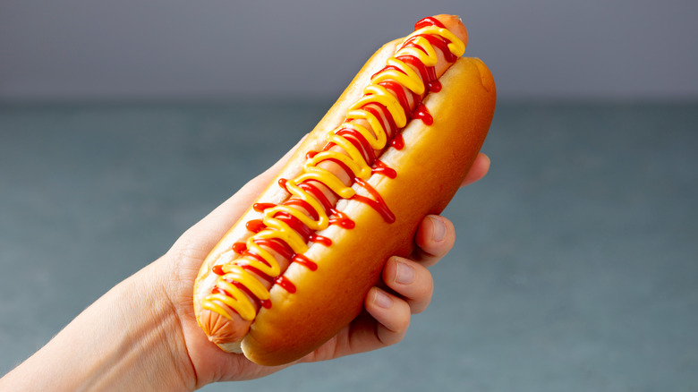 A hand holds a hot dog with ketchup and mustard