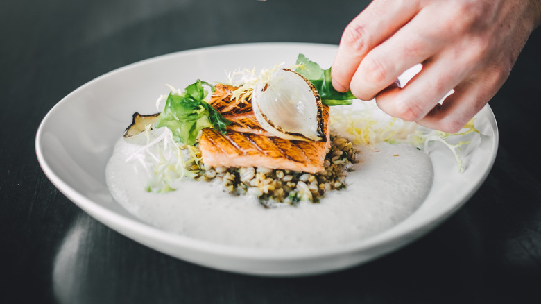 Hands preparing Michelin starred fish on plate