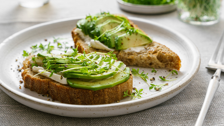 Sliced avocado on two slices of toast on a white plate with a garnish.