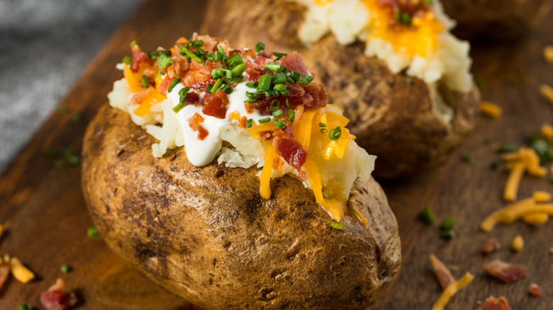 Two loaded baked potatoes topped with sour cream, cheese, bacon, and chives sit on a wooden surface