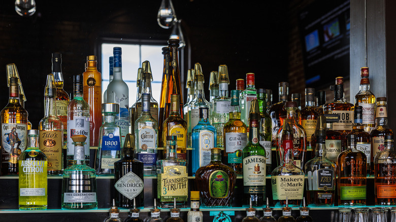 A variety of liquor bottles sit on shelving in front of a mirror