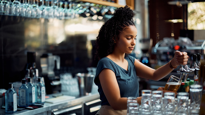 A bartender pours a draft beer behind a bar