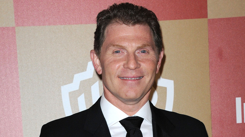 Photo of Bobby Flay smiling in a black suit with a white shirt and black tie