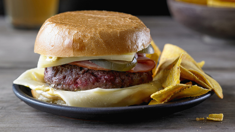 A burger from one of Bobby Flay's restaurants sits on a black plate on a wooden tabletop